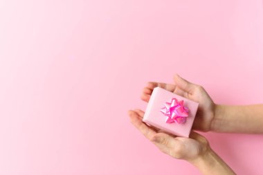 Hands with pink gift box with beautiful rose bow on pink background. St. Valentines day concept. Gift concept. Copy space for your text.