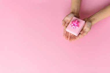 Hands with pink gift box with beautiful rose bow on pink background. St. Valentines day concept. Gift concept. Copy space for your text.