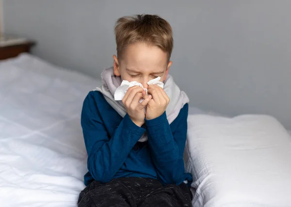 Caucasian 7 year old sick boy blowing his nose. Virus concept.