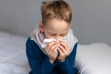 Caucasian 7 year old sick boy blowing his nose. Virus concept.