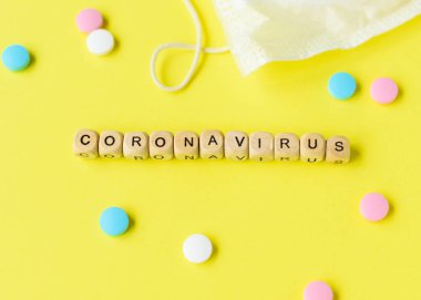 Coronavirus concept. Protective mask, pills and beads with letters on yellow background. Contagious virus concept. clipart