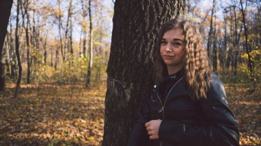 Ağaçların arasında genç bir kadın. Güz bahçesinde dikilip kameraya bakan genç ve çekici bir kadının portresi.