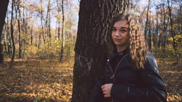 Fiatal nő a fák között. Az őszi kertben álló fiatal, vonzó nő portréja és a kamerába nézés — Stock Fotó