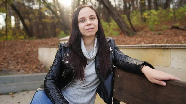 Una joven hermosa mujer con ropa casual está sentada en un banco en el parque de otoño . — Foto de Stock