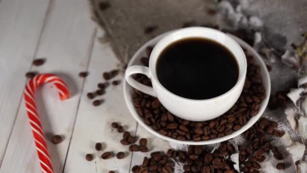 En varm kopp kaffe med godis och kaffebönor på bordet i ett café. Sammansättning av ett gott kaffe och sött mellanmål. — Stockvideo