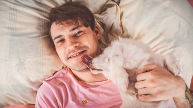 Handsome man lying with dog at bed. Young man in a bed under a rug with his dog in an embrace. Man with dog lying down in the bed in a morning and looking in to a camera