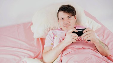 Joystickli bir adam yatakta video oyunu oynuyor. Oyun bağımlısı, oyun bağımlısı, boş vakti olan genç bir erkek.