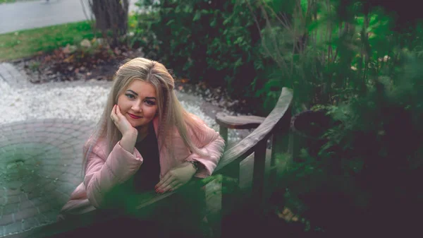 Um retrato de uma mulher bonita, sentada em um banco perto da vegetação verde. — Fotografia de Stock