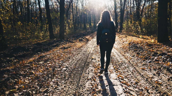 Anonymous woman walking in park. Back view of young female with ornamental backpack walking along path in quiet autumn park — Stock Photo, Image
