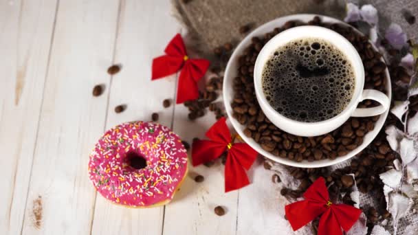 En varm kopp kaffe med en munk och kaffebönorna på bordet. Sammansättning av ett gott kaffe och sött mellanmål. — Stockvideo