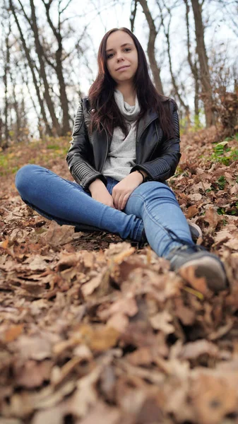 Güz ormanında, uzun saçlı, sıradan giysili hoş bir kadın oturuyor.. — Stok fotoğraf
