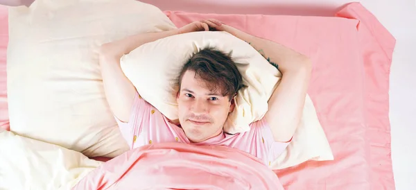 A young handsome man is lying in a bed and enjoying a rest. The man woke up satisfied and happy on his a weekend day. Close up. — Stock Photo, Image