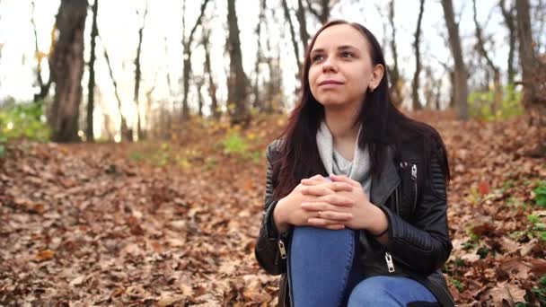 Une jeune femme agréable en vêtements décontractés aux cheveux longs est assise dans la forêt d'automne . — Video