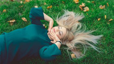 Çimlerin üzerinde yatan güzel bir kızın portresi. Büyüleyici bir kadın yeşil çimlerde yatıyor, sarı yapraklarla..