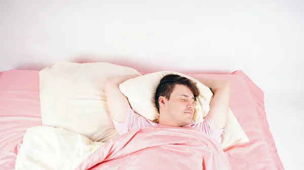 A young handsome man lies in bed and sweetly falls asleep. The man prepared for sleep, closing his eyes and anticipating the pleasant dreams. — Stockfoto
