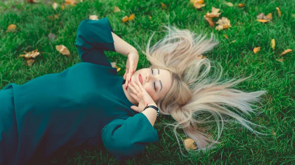 Çimlerin üzerinde yatan güzel bir kızın portresi. Büyüleyici bir kadın yeşil çimlerde yatıyor, sarı yapraklarla..