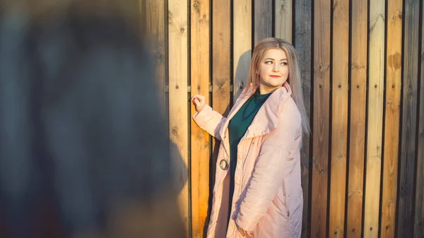 Un ritratto di una bella ragazza, in posa vicino a una recinzione di legno al tramonto in primavera . — Foto Stock