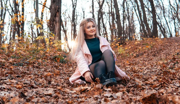 Uma jovem mulher agradável em roupas casuais com cabelos longos está sentada na floresta de outono . — Fotografia de Stock