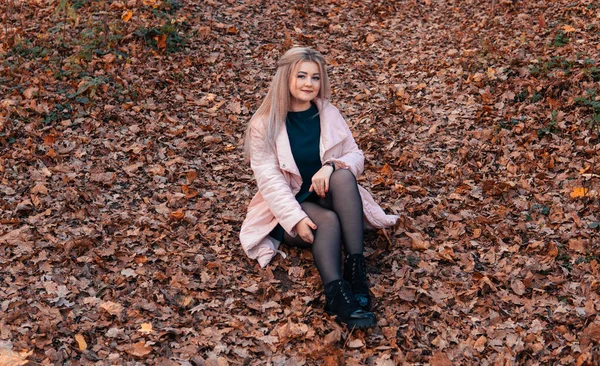 Een jonge aangename vrouw in casual kleding met lang haar zit in het herfstbos. — Stockfoto