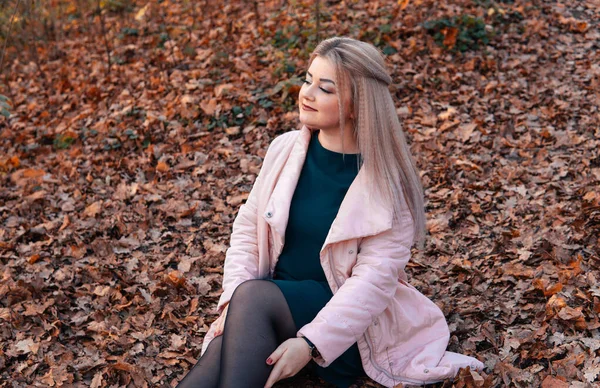 Молодая приятная женщина в повседневной одежде с длинными волосами сидит в осеннем лесу . — стоковое фото