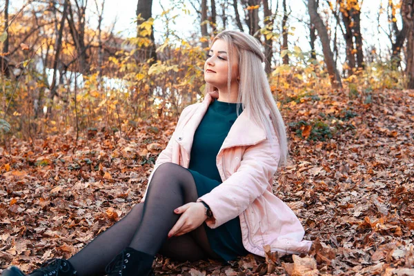 Egy fiatal, kellemes nő alkalmi ruhában, hosszú hajjal ül az őszi erdőben.. — Stock Fotó