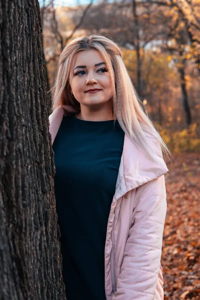 Donna seria che guarda fuori da dietro l'albero. Donna piuttosto calma che tocca l'albero e guarda la fotocamera nella foresta tranquilla — Foto Stock