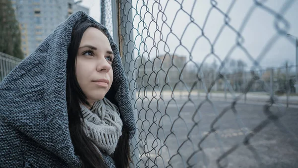 Une jeune belle femme au manteau gris pose près d'une clôture en treillis à la fin de l'automne . — Photo