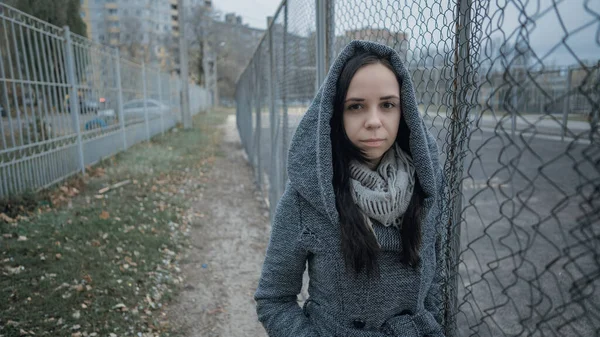 Uma jovem mulher bonita no casaco cinza posa perto de uma cerca de treliça em um final de outono . — Fotografia de Stock