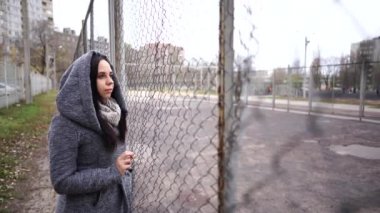 Gri montlu güzel bir kadın sonbaharın sonlarında çitin yanında poz veriyor.