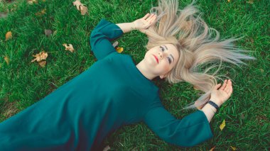 Çimlerin üzerinde yatan güzel bir kızın portresi. Büyüleyici bir kadın yeşil çimlerde yatıyor, sarı yapraklarla..