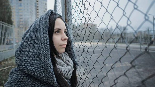 Uma jovem mulher bonita no casaco cinza posa perto de uma cerca de treliça em um final de outono . — Fotografia de Stock