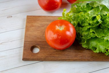 Su damlacıkları ve yeşil marullu kırmızı domatesler tahta bir tahtanın üzerinde..