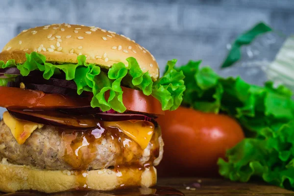 Um hambúrguer suculento enorme está em uma tábua de corte em um fundo de tijolo cinza . — Fotografia de Stock