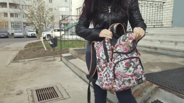 Mladá žena drží batoh a snaží se v něm něco najít na nádvoří města..
