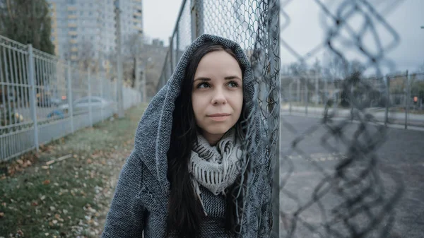 Uma jovem mulher bonita no casaco cinza posa perto de uma cerca de treliça em um final de outono . — Fotografia de Stock