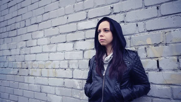 Siyah deri ceketli kadın. Hüzünlü kadın yana bakıyor. Tuğla duvarın arkasında siyah deri ceketli genç bir kadın. — Stok fotoğraf