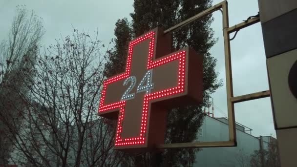 Фармацевтический знак, знак или символ аптеки с красным крестом на фасаде здания с улицы на фоне облачного неба — стоковое видео