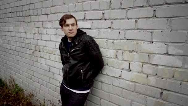 Man in a black leather jacket. Sad male looking to the side. Young man in a black leather jacket at the background of a brick wall — Stock Video