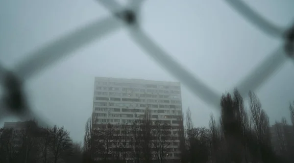 Αστικό υπόβαθρο της πόλης. Πολυώροφο κτίριο το πρωί, στην ομίχλη. Κτίριο διαμερισμάτων πίσω από τα κάγκελα. Γκέτο, στεγάζει τους φτωχούς. Έννοια: περιορισμός της ελευθερίας — Φωτογραφία Αρχείου