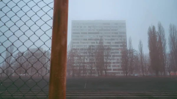 Αστικό υπόβαθρο της πόλης. Πολυώροφο κτίριο το πρωί, στην ομίχλη. Κτίριο διαμερισμάτων πίσω από τα κάγκελα. Γκέτο, στεγάζει τους φτωχούς. Έννοια: περιορισμός της ελευθερίας — Φωτογραφία Αρχείου