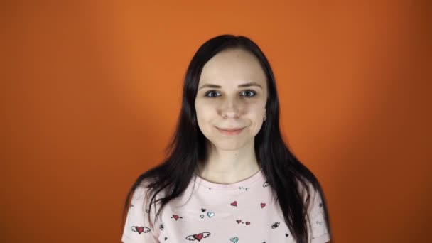 Hermosa mujer sonriendo mirando a la cámara de pie en un fondo naranja.. — Vídeos de Stock