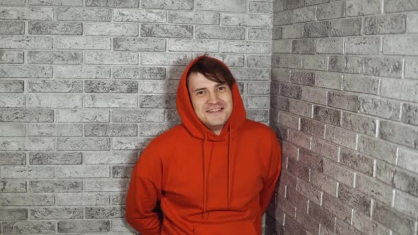 Um homem emocional bonito em um hoodie vermelho é surpreendido feliz com as mãos em suas bochechas. — Vídeo de Stock