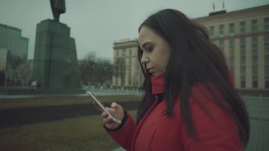 Genç ve güzel bir kadın meydanda duruyor ve sosyal ağdaki çeşitli haberlere cep telefonuyla bakıyor..