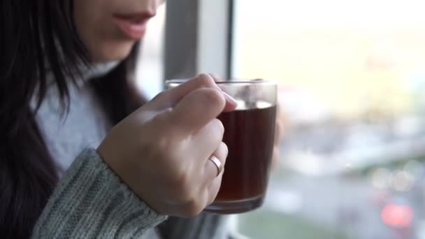 Cierre, mujer en un jersey gris bebe un té, mirando hacia la ventana en el balcón.. — Vídeo de stock