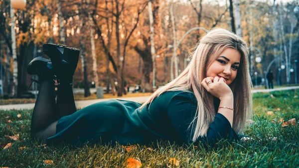 Portrét krásné dívky, ležící na trávě. Okouzlující žena leží na zelené trávě se žlutými listy. — Stock fotografie