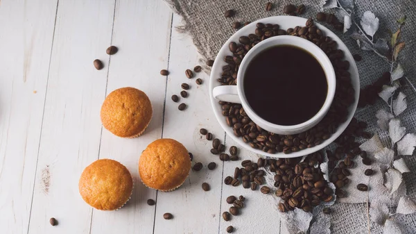 Горячая чашка кофе с кофейными зернами и маленькими кексами на столе. Состав вкусного кофе и сладких закусок . — стоковое фото