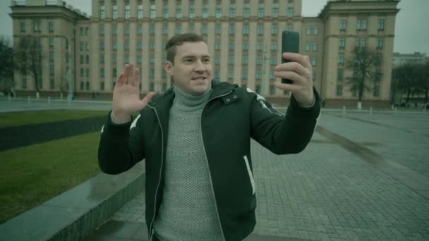 Un jeune bel homme en vêtements décontractés effectue une diffusion en direct sur son téléphone portable dans une place au centre de la ville . — Video