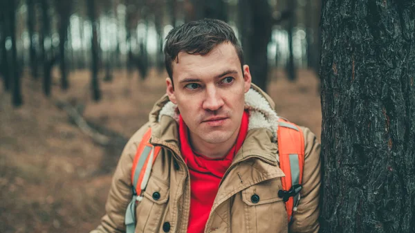 A traveling man with map in woods. A portrait of the handsome man with a backpack, standing near a tree in a cold weather. — Stock Photo, Image