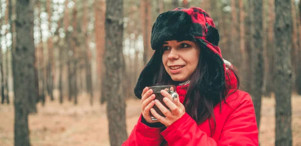 一个漂亮女人的肖像，在树林里喝杯茶。穿着夹克、头戴耳环的女人在寒冷的天气里喝茶. — 图库照片