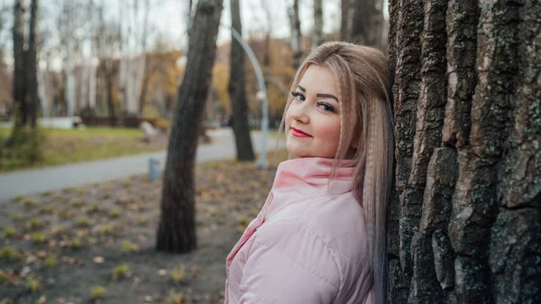 Donna che guarda fuori da dietro l'albero. Bella donna calma toccando albero e guardando la macchina fotografica in foresta tranquilla — Foto Stock